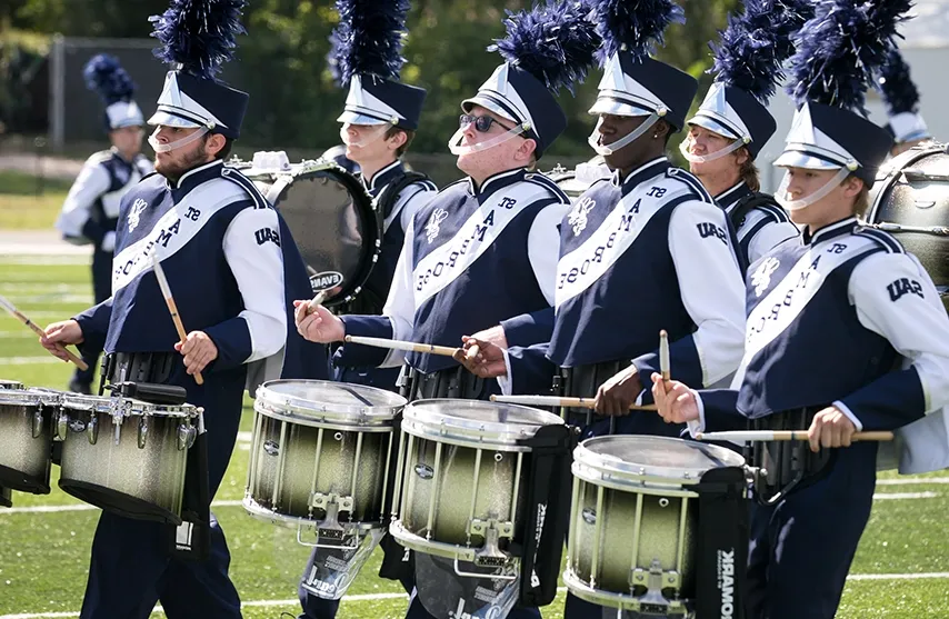 A line of drum majors drum in unison.