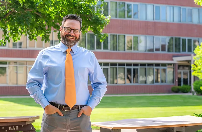 Jason Richter stands in front of a university building and under a tree.