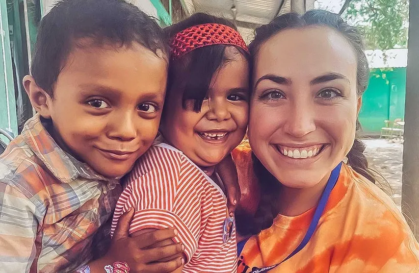 A woman in an orange shirt takes a selfie with two children.